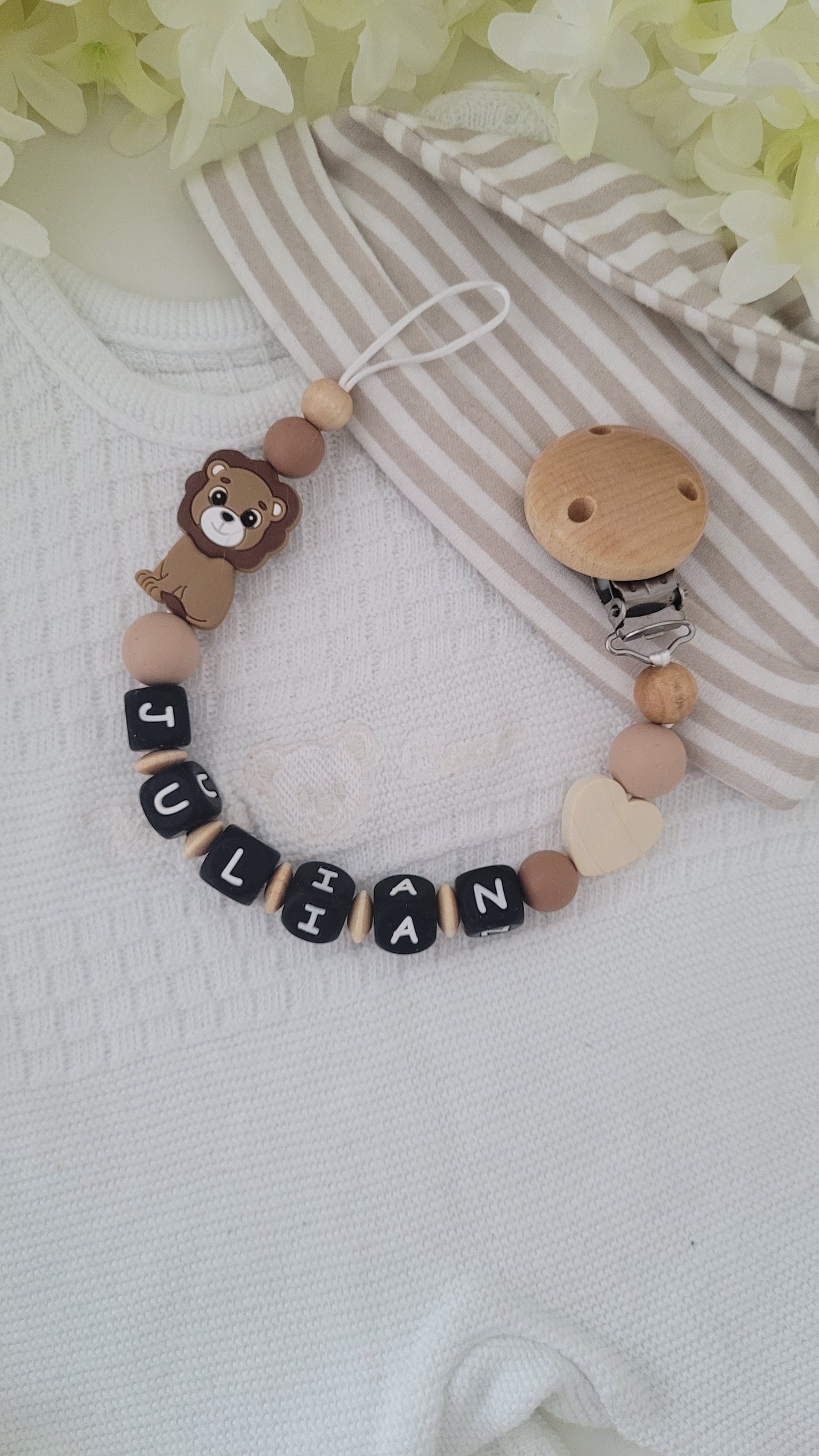 Schnullerkette personalisiert aus Silikonperlen und Holzperlen mit einem Holzherz und Silikonlöwen Motivperle Name in schwarzen Silikonbuchstaben